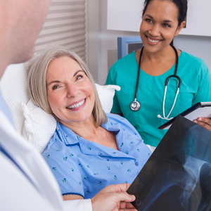 photograph of smiling woman in hospital bed talking to a doctor.