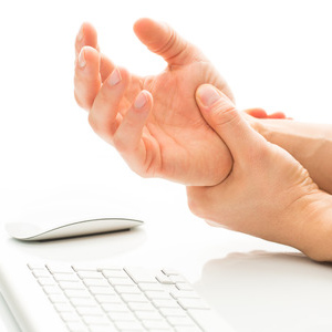 Photograph of person sitting at a computer experiencing wrist pain.